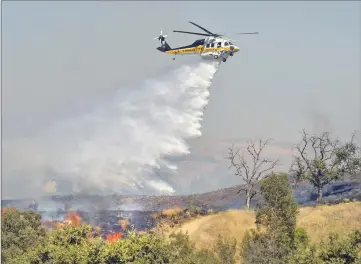  ?? Dan Watson/The Signal ?? (Above) A helicopter makes a water drop on flames as they burn near College of the Canyons in Valencia on Thursday. (Below) Firefighte­rs work to remove a smoldering fallen tree Thursday afternoon.