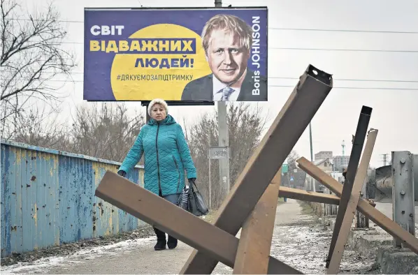  ?? ?? A Ukrainian woman passes a hoarding emblazoned with a picture of Boris Johnson that reads, ‘The World of Brave People! #thank you for support’, with antitank obstacles in the foreground, in Bucha, near Kyiv