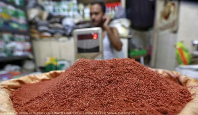  ?? ?? A shopkeeper speaks on his mobile phone next to a sack filled with potash for sale in Kolkata. Image: Reuters