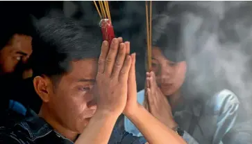  ??  ?? Worshipper­s at the Jade Emperor Pagoda clasp incense sticks together.