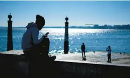  ?? ARMANDO FRANCA/AP ?? A young man checks his phone Jan. 30 by the Tagus River in Portugal.