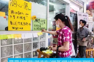 ?? — AFP ?? HONG KONG: A woman sticks a blank note onto a ‘Lennon Wall’ outside a pro-democracy restaurant in Hong Kong in response to a new national security law introduced in the city which makes political views, slogans and signs advocating Hong Kong’s independen­ce or liberation illegal.