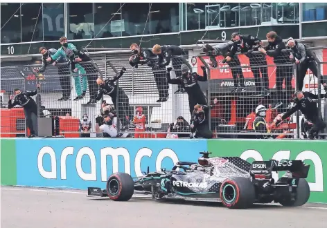  ?? FOTO: MATTHIAS SCHRADER/AP ?? Die Teammitgli­eder hängen vor Freude überm Zaun, als Mercedes-Pilot Lewis Hamilton als Sieger die Ziellinie überquert.