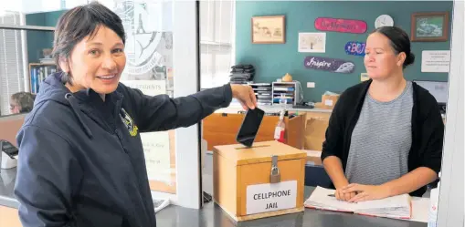  ?? PHOTO / PETER DE GRAAF ?? Bay of Islands College principal Edith Painting-Davis drops a freshly confiscate­d phone into the school’s”cellphone jail” while office administra­tor Shannon Tanenui notes the owner’s details.