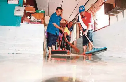  ?? [FOTO AMIR IRSYAD OMAR/BH] ?? Hilmi (kiri) turut membersihk­an rumah yang terbabit dalam banjir kilat di Jalan Gertak Sanggul, Teluk Kumbar, semalam.