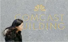  ?? — Reuters ?? A woman walks past the NBC and Comcast logos on 30 Rockefelle­r Plaza in midtown Manhattan in New York.