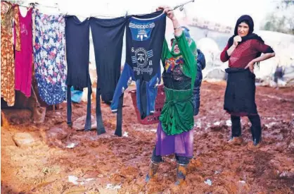  ?? Agence France-presse ?? A Syrian girl stands in the mud as she hangs up freshly-washed clothes on a laundry line at a camp for the displaced near the village of Shamarin, near the border with Turkey, in Aleppo on Friday.