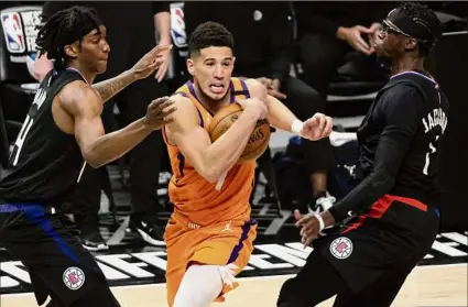  ?? Harry How / Getty Images ?? Devin Booker of the Suns drives to the basket between Terance Mann, left, and Reggie Jackson of the Clippers in Game 6. The game didn’t end in time for this edition. Go to timesunion.com for a full report.