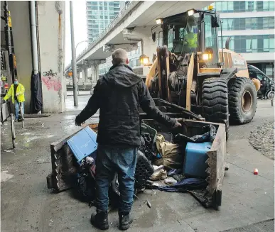  ??  ?? Jason Phillips gestures to the driver of a city truck who attempts to remove Phillips’ belongings as workers move to clear an encampment on Toronto’s Bay Street on Friday.