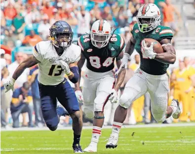  ?? CHARLES TRAINOR JR./MIAMI HERALD ?? Miami Hurricanes Mark Walton (1) runs for a first-quarter touchdown as Toledo Rockets Ka’dar Hollman (13) trails at Hard Rock Stadium in Miami Gardens on Saturday.