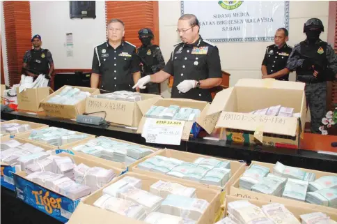  ??  ?? Mustafar (centre) showing the RM13.5 million cash discovered by immigratio­n officers during the raid at a hotel spa and an apartment.