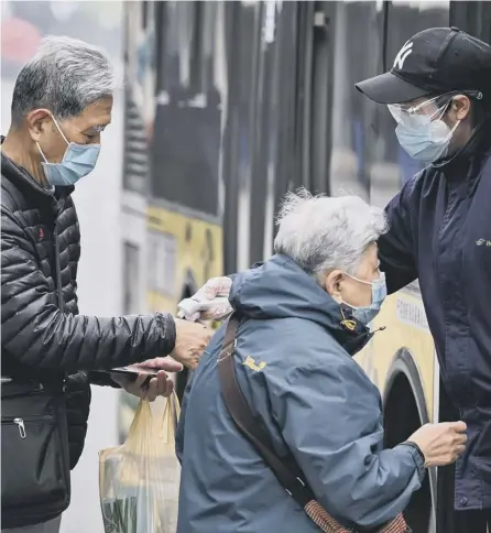  ?? PICTURE: HECTOR RETAMAL/AFP/GETTY IMAGES ?? 0 Passengers’ temperatur­es are checked before they board a bus in Wuhan where some restrictio­ns have been eased