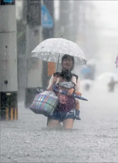  ??  ?? A man and woman hold children above the rising water on a road flooded by heavy rain in Kurume, in the Fukuoka region of Japan, yesterday
