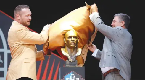  ?? JOE ROBBINS/GETTY IMAGES ?? Brian Urlacher and former defensive coordinato­r Bob Babich unveil Urlacher’s Hall of Fame bust before his speech Saturday.