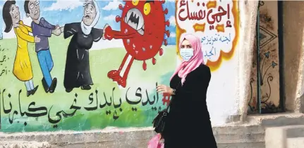 ?? ADEL HANA/ASSOCIATED PRESS FILE ?? A woman walks past a mural encouragin­g the wearing of face masks amid the coronaviru­s pandemic, on the main road of Nusseirat refugee camp, central Gaza Strip. In Arabic it reads: “protect yourself, together we protect the old.”