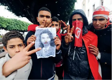  ??  ?? Des jeunes font le V de la victoire avec une image taguée de Leïla Trabelsi, le 27 janvier 2011 à Tunis.