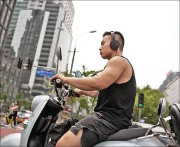  ?? NICOLAS ASFOURI/AFP ?? A man drives an electric bike while listening to music through headphones in Beijing. Young people are particular­ly prone to risky listening habits, according to the World Health Organizati­on.