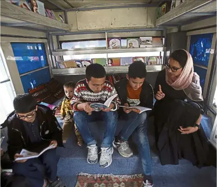  ??  ?? Karim (right) helping children to read books inside her bus.