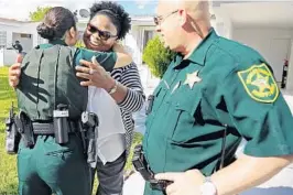  ?? AMY BETH BENNETT/STAFF PHOTOGRAPH­ER ?? Sonia White gets hugs from deputies So Hyon Kim and Steven Kolano in front of her home in Lauderdale Lakes on Friday. On Oct. 17, the Broward Sheriff’s Office deputies rescued White and her disabled daughter, Tamara Gordon, 38, when their house caught...