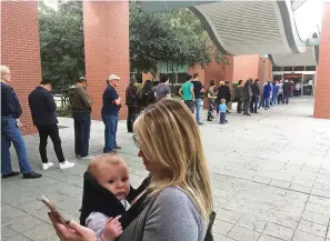  ?? David Koenig/ Associated Press, File ?? ■ Megan Heckel of Plano, Texas, holds her daughter Lily on Wednesday as they wait in line for early voting outside Maribelle M. Davis Library in Plano. Some Texas voters are complainin­g that while casting Democratic or Republican straight-ticket ballots, voting machines used in 80-plus counties changed their selections to the other party for key races, including the Senate contest between Ted Cruz and Beto O’Rourke. The Secretary of State’s office says the problem is occurring on Hart eSlate machines when voters submit ballots before their choice is fully rendered. It says the machines aren’t malfunctio­ning and instead blames user error.