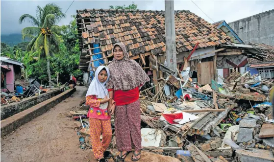  ??  ?? A girl and her mother in front of a collapsed house in Rajabasa in Lampung province on December 25, 2018, following the deadly tsunami that hit off the Indonesian island of Java.