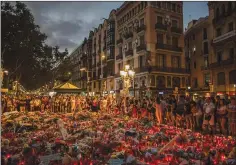  ?? AP PHOTO SANTI PALACIOS ?? People stand next to candles and flowers placed on the ground in Barcelona, Spain, Monday. The lone fugitive from the Spanish cell that killed 15 people was shot to death Monday after he flashed what turned out to be a fake suicide belt at two troopers...