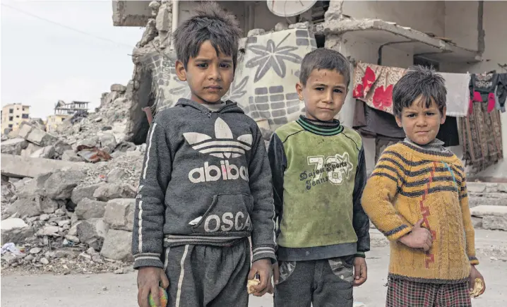  ??  ?? Displaced children stand in front of the bomb-damaged building in which they now live, while, right, Abdul Karim, 55, brews tea on the building site he guards. Below: activist Maria al-Ojeili at her home in Raqqa