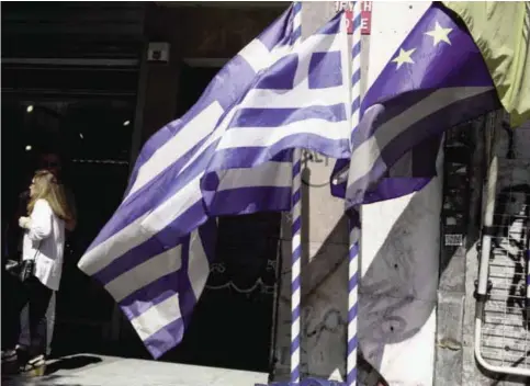  ?? —AP ?? ATHENS: A woman walks past European and Greek flags in Athens yesterday.