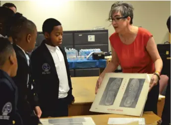  ?? ANDY GRIMM/ SUN- TIMES ?? Kara Stefanson, a forensic scientist for the Cook County state’s attorney’s office, asks middle school students — including Tyrus Johnson, Corey Moses Jr. and Khaleel Williams — to compare shoe prints during a session on forensic evidence.