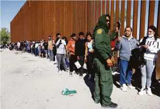  ?? Mario Tama / Getty Images ?? A U.S. Border Patrol agent in Yuma, Ariz., checks for identifica­tion as immigrants wait in line to be processed after crossing from Mexico on May 21.