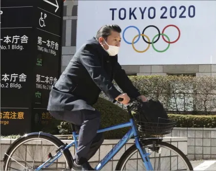  ?? KOJI SASAHARA ?? A man wearing a face mask cycles past the logo of the Tokyo Olympics, in Tokyo, Wednesday, Feb. 17, 2021. The Olympics are scheduled to open on July 23 but recent polls show about 80% of the Japanese public want the Olympics canceled or postponed. Gov. Tatsuya Maruyama of Shimane prefecture, western Japanese, is talking about canceling the torch relay events in his area for the Tokyo Games, reported on Wednesday. Maruyama is unhappy with COVID-19 prevention measures surroundin­g the relay.