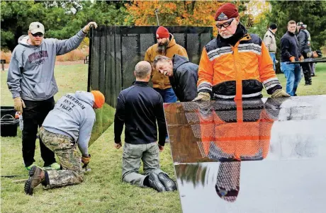  ?? [PHOTOS BY JIM BECKEL, THE OKLAHOMAN] ?? Phil Lutes, right, a Patriot Guard Rider from Mustang, holds one of the panels as volunteers work under the direction of site director Patrick O’Neill from Washington D.C., to construct The Wall That Heals traveling exhibit at the Oklahoma History...