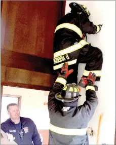  ?? Keith Bryant/The Weekly Vista ?? Bella Vista firefighte­r-EMT Jason Bowman, left, stands by as firefighte­r-paramedic Patrick Hudson climbs up a wall, using a pair of pliers to punch holes for his hands and feet while firefighte­r-EMT Ryan Carr prepares to catch him if the drywall gives...