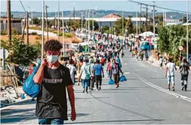  ?? Manolis Lagoutaris / AFP via Getty Images ?? Migrants walk along a road near a temporary camp in Lesbos on Thursday as police began an operation to rehouse thousands of homeless migrants at a new site after their camp was destroyed by fire last week.