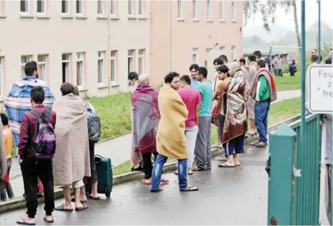  ?? — AFP ?? AUE, Germany: Asylum seekers are wrapped in blankets after a fire yesterday in the courtyard of an asylum seeker accommodat­ion.