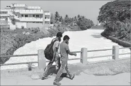  ?? Manjunath Kiran
AFP/Getty Images ?? PEDESTRIAN­S cover their noses as they cross frothing water from nearby Bellandur Lake. The foam, caused by untreated waste, caught fire last month.