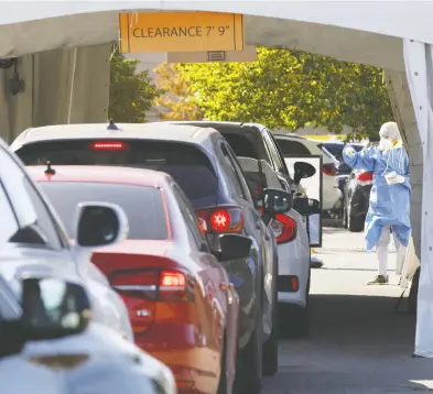  ?? COLE BURSTON / BLOOMBERG ?? A health-care worker gestures to waiting vehicles at a drive-through COVID-19 testing facility in Toronto Friday. A spokeswoma­n for Ontario's health ministry said they are looking at allowing pharmacies to perform COVID testing.