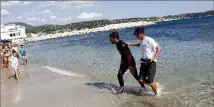  ??  ?? Rémi Camus, aidé par un bénévole accompagna­teur, pose les pieds sur le sable après un peu moins de  h de nage en mer.