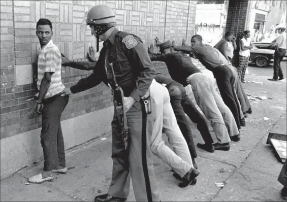  ?? THE ASSOCIATED PRESS FILE ?? A Michigan State police officer searches a youth on Detroit’s 12th Street where looting was still in progress after the previous day’s rioting. The last surviving member of the Kerner Commission says he remains haunted that the panel’s recommenda­tions...