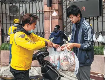  ?? HE DONGPING / FOR CHINA DAILY ?? A deliveryma­n hands over food at a school entrance in Shanghai.