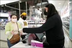  ?? PHOTOS BY CHARLES REX ARBOGAST — THE ASSOCIATED PRESS ?? Cashier Druhan Parker, right, works behind a plexiglass shield Thursday, as he checks out shoppers Cassie Howard, left, and Paris Black at an in Chicago.