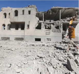  ?? (Reuters) ?? A Houthi gunman walks by a Houthi-run detention center hit by air strikes in Sanaa earlier this week.