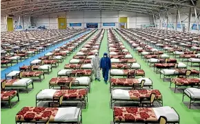  ?? AP ?? People in protective clothing walk past rows of beds at a temporary 2000-bed hospital for Covid-19 patients set up by the Iranian army at the internatio­nal exhibition center in northern Tehran.