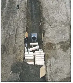  ?? (File Photo/AP/John Minchillo) ?? Workers wearing personal protective equipment bury bodies of covid-19 victims in a trench on Hart Island in the Bronx borough of New York on April 9.