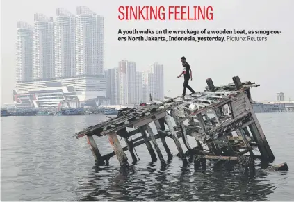  ?? Picture: Reuters ?? A youth walks on the wreckage of a wooden boat, as smog covers North Jakarta, Indonesia, yesterday.