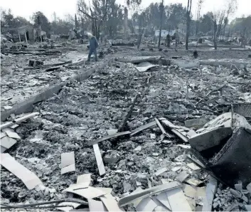  ?? JEFF CHIU/THE ASSOCIATED PRESS ?? Phil Rush walks through the burnt remains at the site of his home destroyed by fires in Santa Rosa, Calif., Wednesday. Wildfires tearing through California’s wine country continued to expand Wednesday, destroying hundreds more homes and structures and...