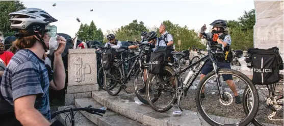  ??  ?? Chicago police protect the statue of Christophe­r Columbus in Grant Park on Friday as protesters crowd around and projectile­s fly through the air.