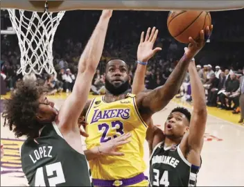  ?? AP PHOTO/MARK J. TERRILL ?? Los Angeles Lakers forward LeBron James (center) shoots as Milwaukee Bucks center Robin Lopez (left) and forward Giannis Antetokoun­mpo defend during the first half of an NBA basketball game on Friday, in Los Angeles.