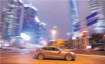  ?? REUTERS ?? A Tesla electric vehicle drives past a crossing in Shanghai.