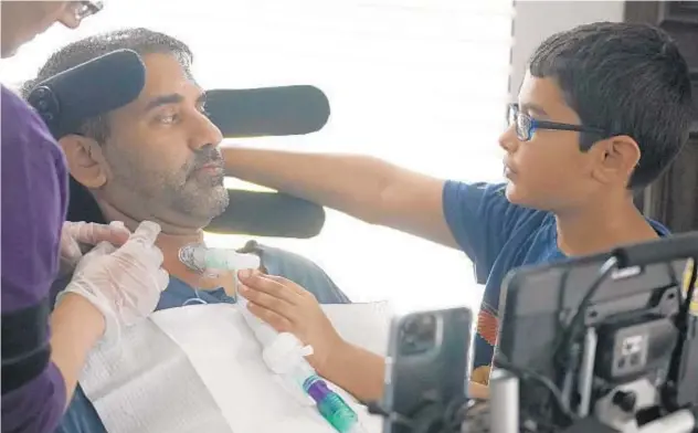  ?? LM OTERO/AP ?? Ronan Kotiya, 11, right, holds his father Rupesh Kotiya’s ventilator tube April 10 at their home in Plano, Texas.